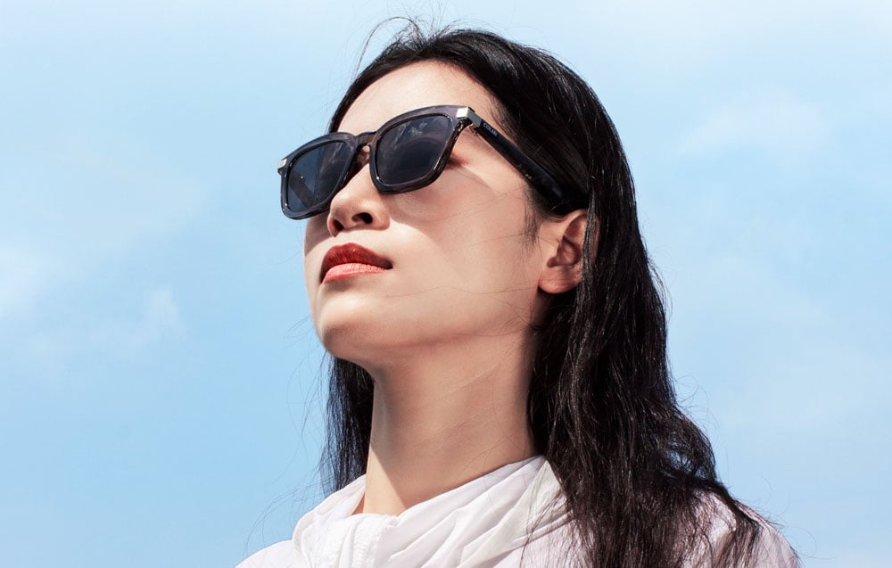 A woman in profile wearing smart glasses against a bright sky.