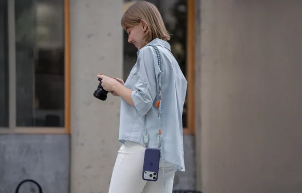 A short-haired woman holds a camera while she has a PGYTECH strap with a smartphone mounted on her shoulder