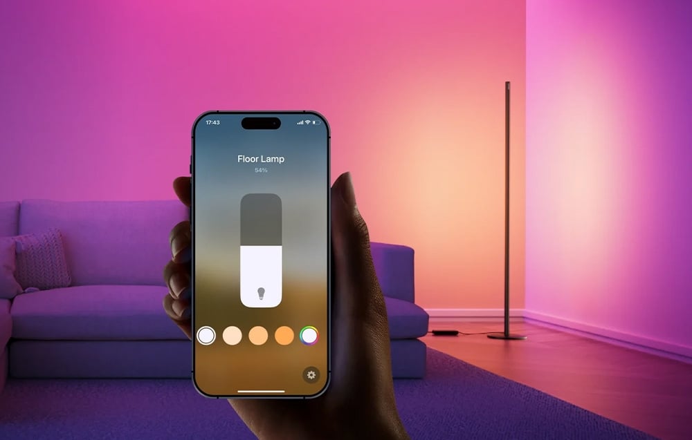 Smartphone controlling colorful LED floor lamp with mobile app in purple-pink room