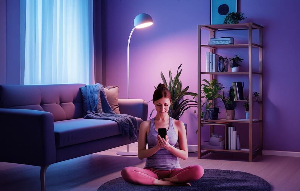 A woman sitting cross-legged on a rug next to a blue sofa holds a smartphone in her hands.