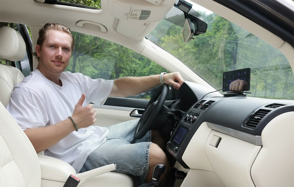 A man in a white T-shirt sits in the car and gives a thumbs-up next to the mounted screen