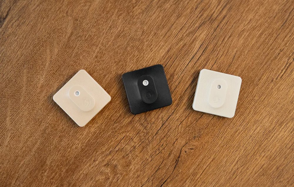 Three color variants of the Shelly H&T; sensor (beige, black, white) placed side by side on a wooden countertop.