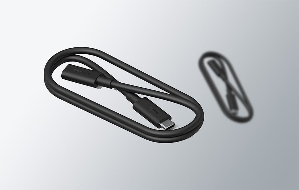 A coiled black USB-C cable by VITURE lies next to its fuzzy reflection on a light background