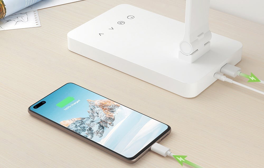 A close-up of the lamp’s base with a connected USB cable charging a smartphone lying on the tabletop