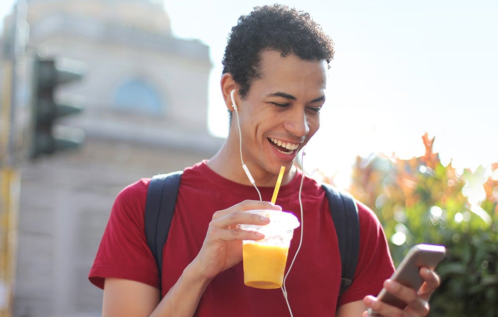 A smiling man holding a smartphone and a cup of juice