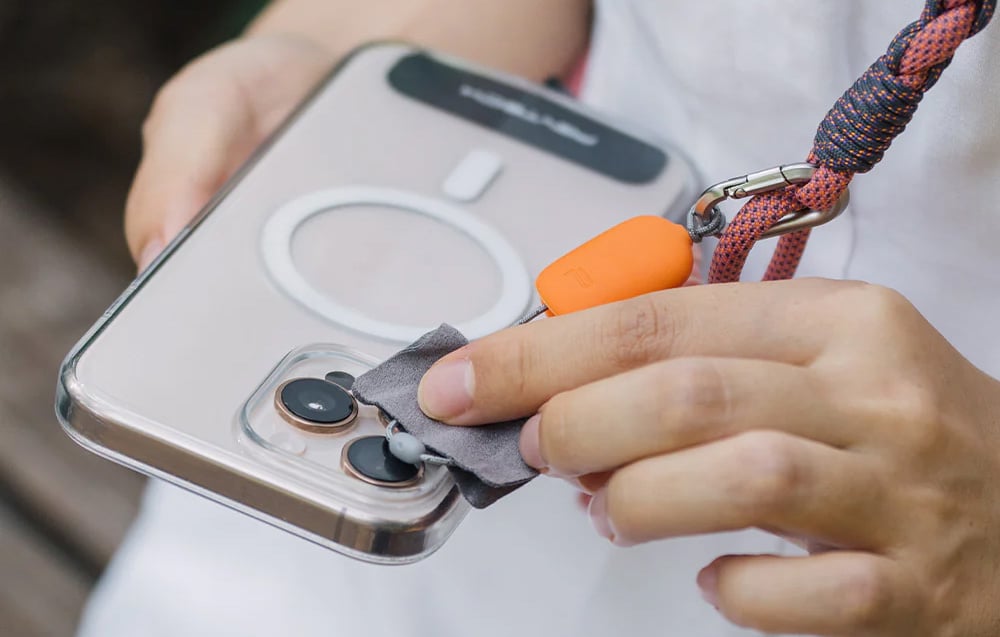 A person cleaning the lens of his smartphone with an orange cloth embedded in the PGYTECH strap