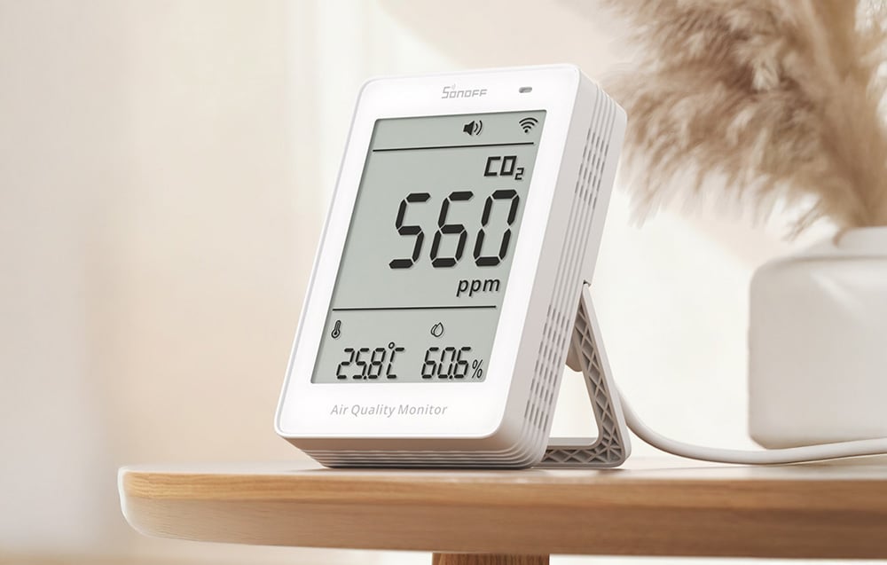 Sonoff air quality meter on a wooden shelf, with a plant in a vase in the background