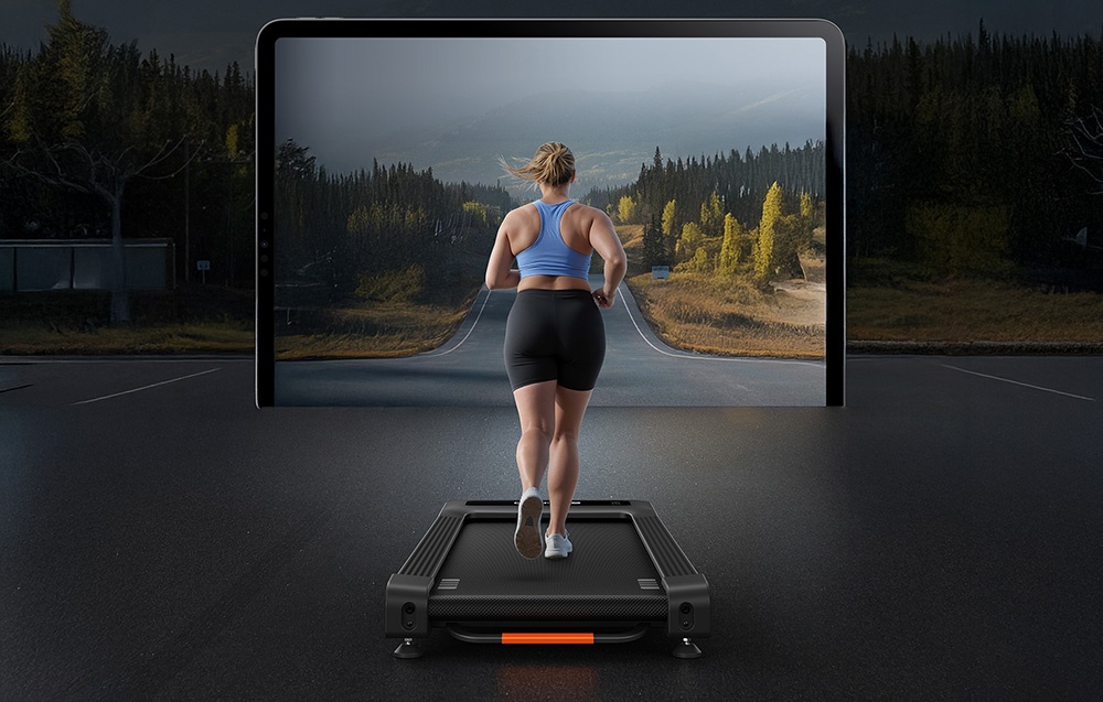 A woman running on a black treadmill toward a large screen displaying a path and a forest