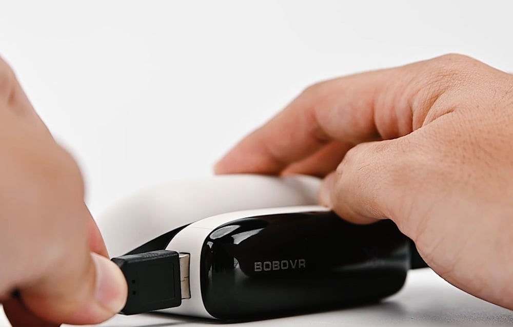 Close-up of hands connecting the cable to the BoboVR PD100 module.