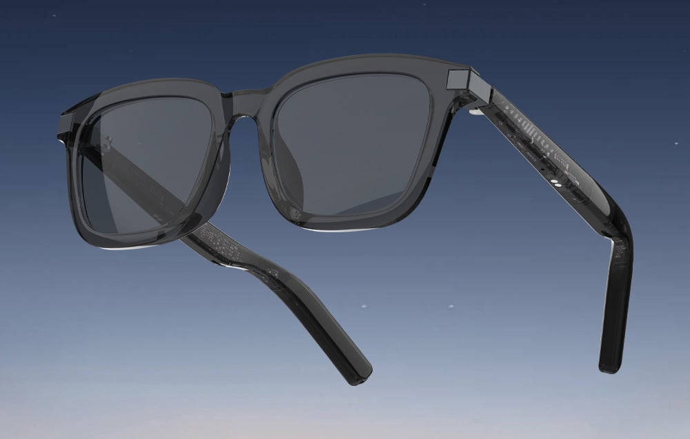 Smart glasses with dark lenses and translucent frames on a blue background.