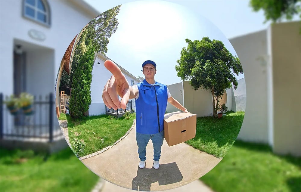 Fish-eye camera view of a courier in a blue vest holding a package and pointing his finger toward the lens