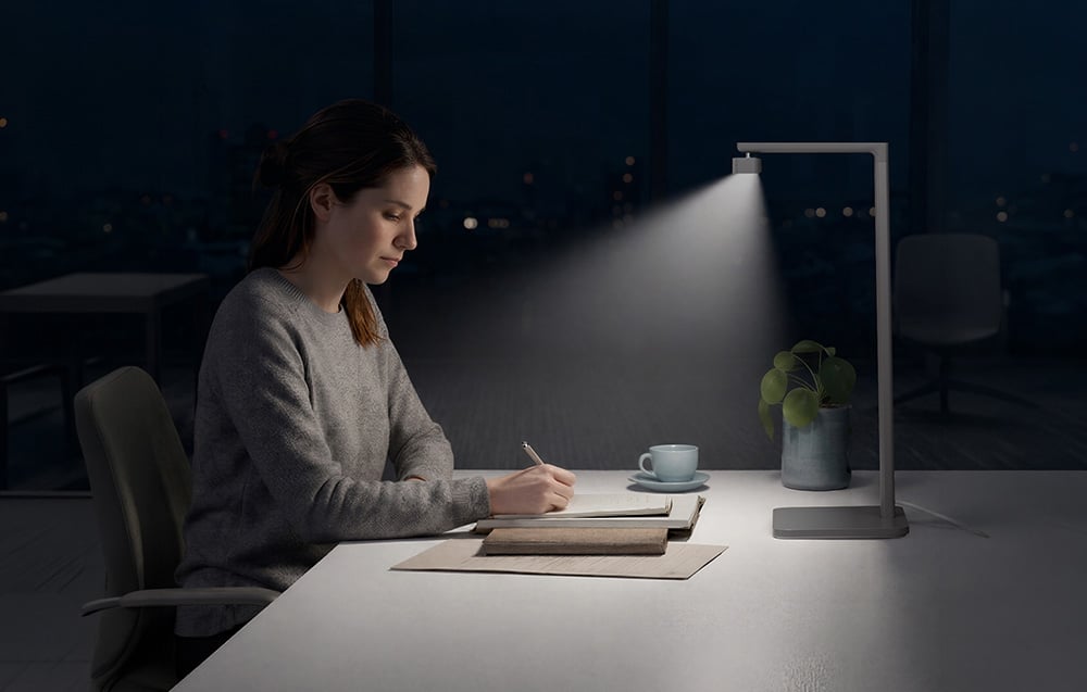 A woman writing in a notebook at a desk illuminated by the bright, focused light of an LED lamp at night