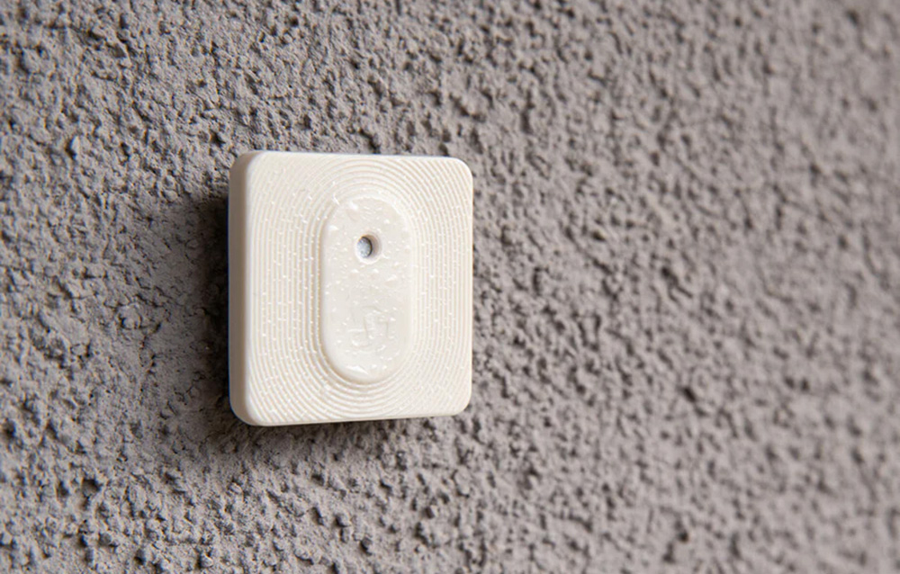 A damp Shelly H&T; sensor mounted on a gray, rough building facade, demonstrating its resistance to outdoor conditions.