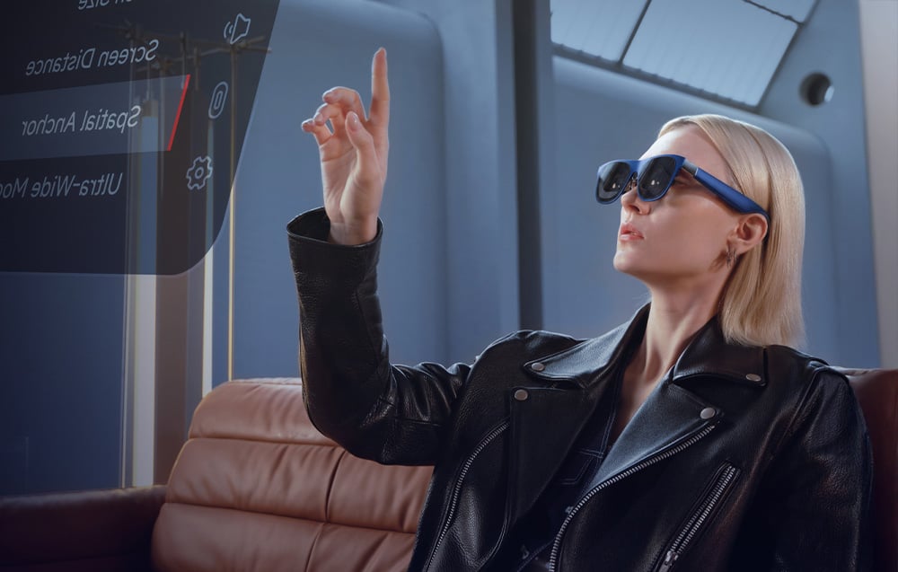 A woman in a black jacket sits on a couch using AR glasses