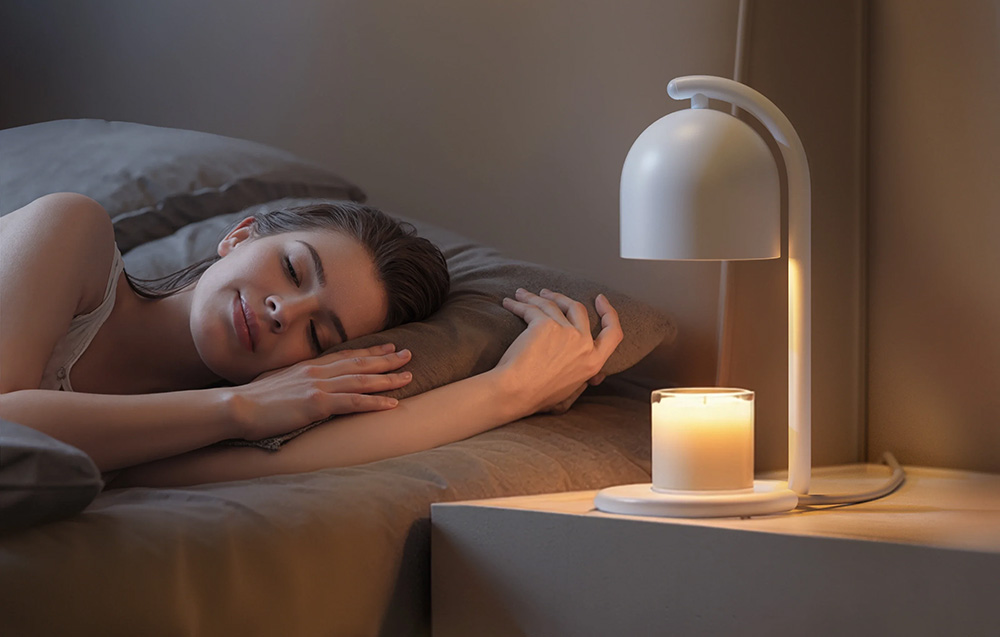 A woman is sleeping in bed, and on the nightstand next to her stands a white candle warmer heating a white scented candle in a glass container, gently illuminat