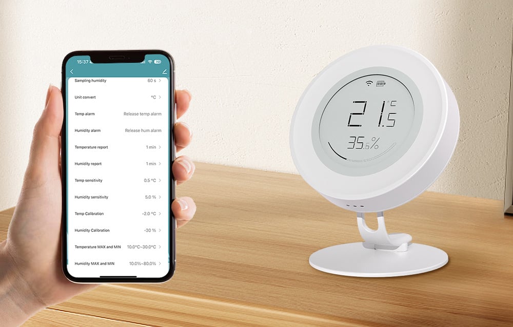 Sensor on a countertop next to a smartphone with temperature and humidity parameter settings in the app