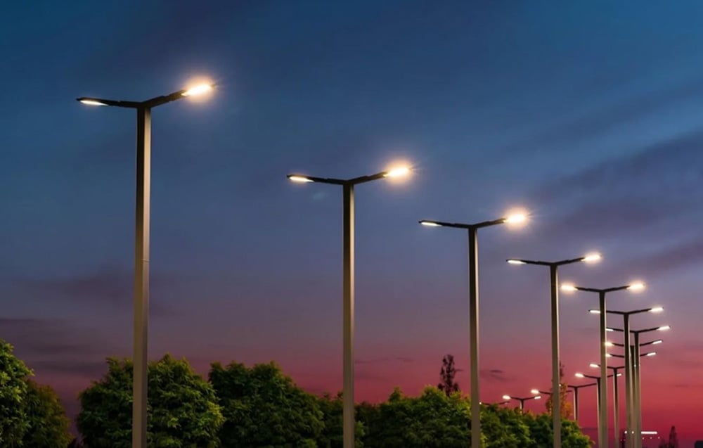 A row of tall, glowing streetlights against the backdrop of the evening sky