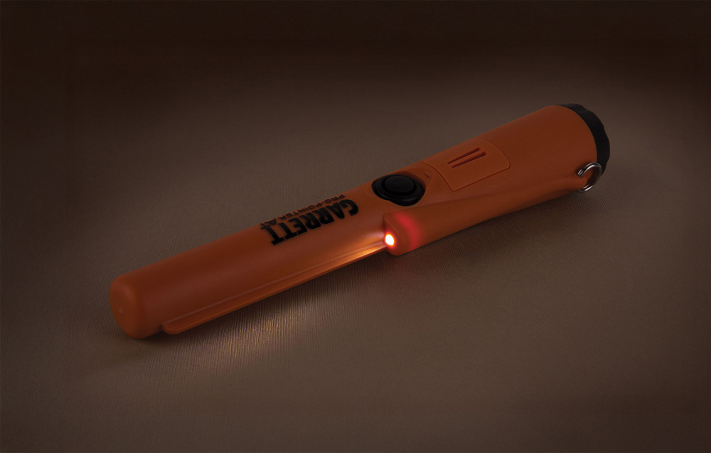 Handheld metal detector with light on against dark background.