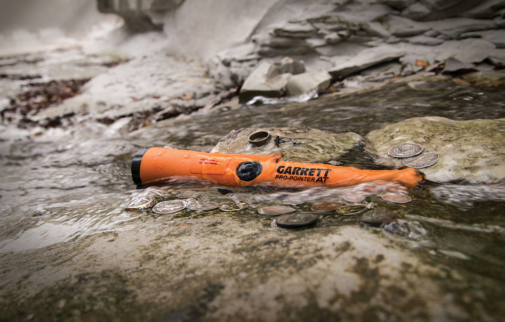 The metal detector lies in the water among coins and rings.
