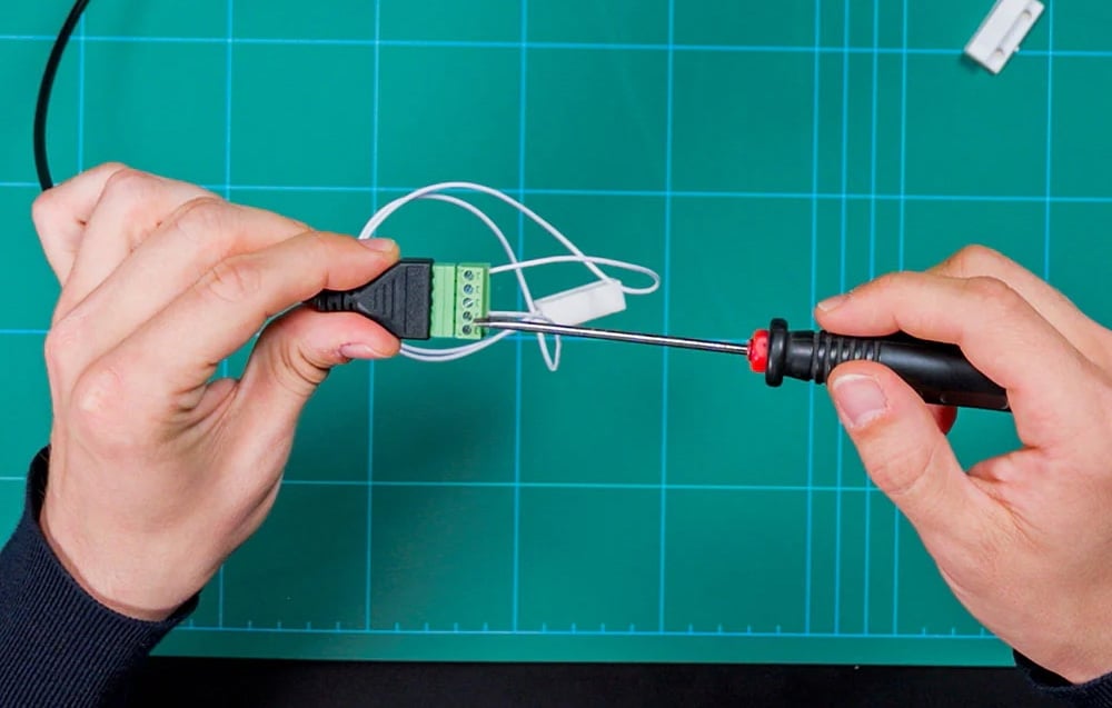 Hands using a screwdriver on a 5-pin Shelly terminal block on a green background